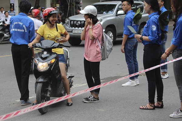 Sinh viên tình nguyện tiếp sức mùa thi đứng trước cổng trường hướng dẫn chỗ gửi xe cho học sinh và phụ huynh.
