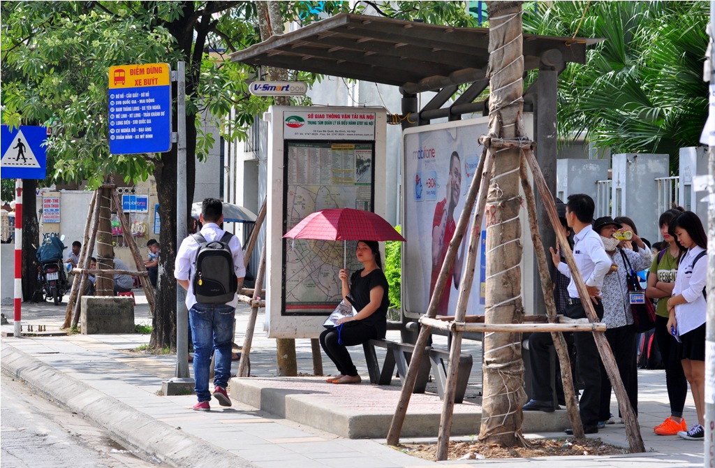 Tại một điểm xe buýt trên đường Nguyễn Chí Thanh, mọi người phải “trốn” phía sau nhà chờ tránh nắng, để đợi xe.