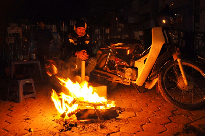 Một anh xe ôm trên đường Lê Hữu Thọ đang ngồi cạnh đống lửa trên vỉa hè khi ngồi đón khách.
