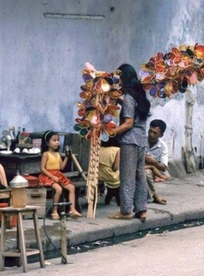 Hà Nội thập niên 1990, một cô bán đèn cù quay đang “chào hàng” với một bé gái bên quán nước.