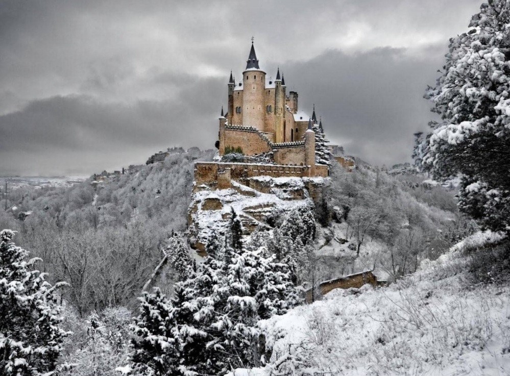 Lâu đài Segovia (Tây Ban Nha) nằm trên ngọn đồi cao, xung quanh là cây cối phủ tuyết trắng.