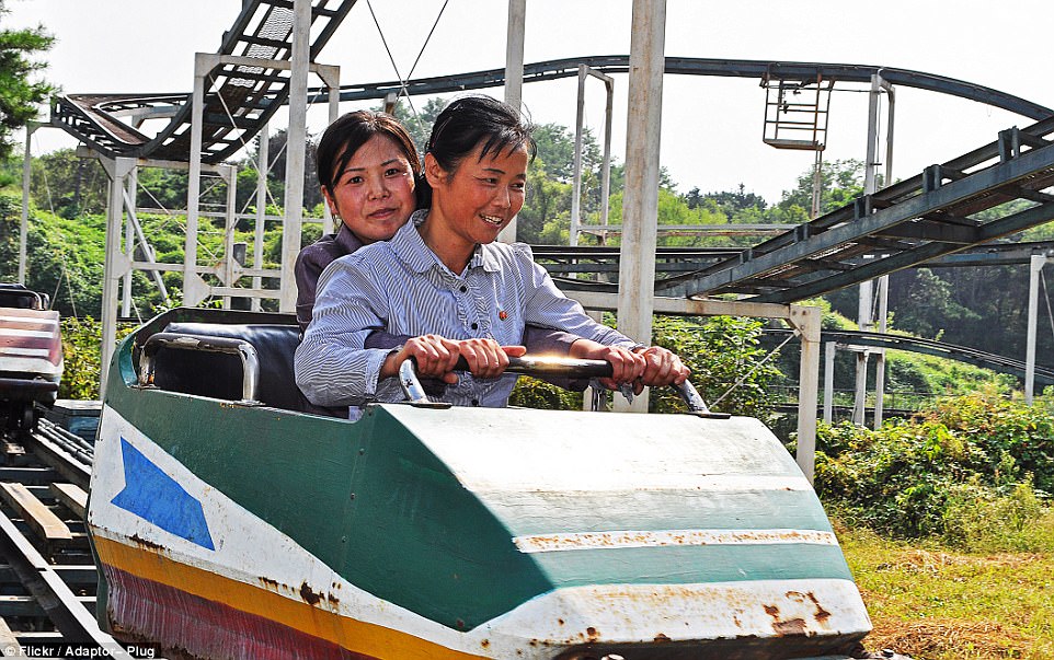 Những người dân Triều Tiên đang rất thích thú bám vào một chiếc tàu lượn siêu tốc, trong khi trẻ em đang được thử chơi bắn cung ngoài trời.