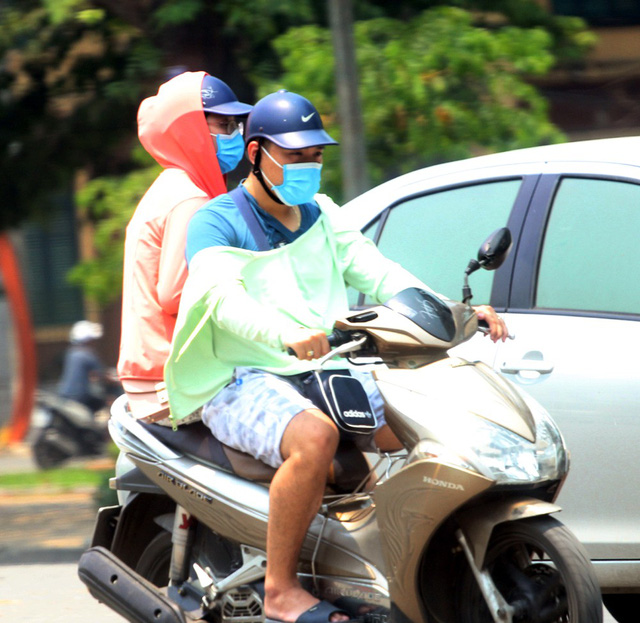 Đôi vợ chồng trẻ chở nhau bằng xe máy phải sử dụng áo chống nắng che chắn phần tay.